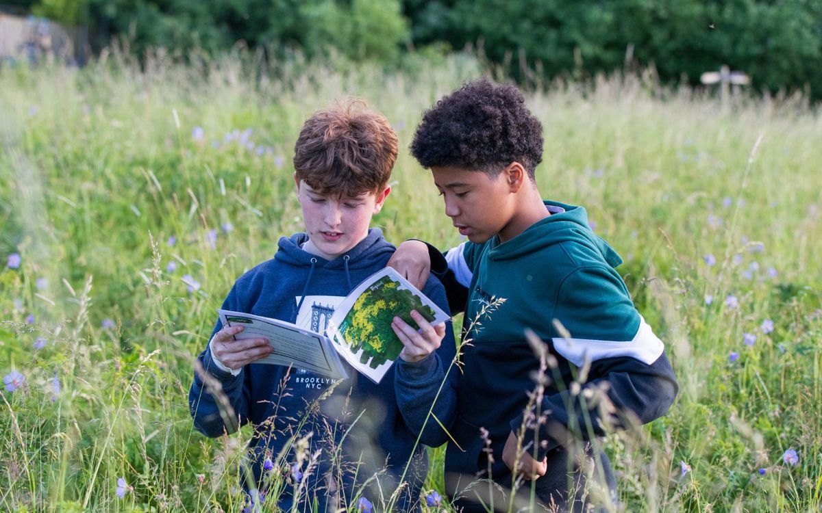 Two teenagers looking at booklet whilst stood in long grass