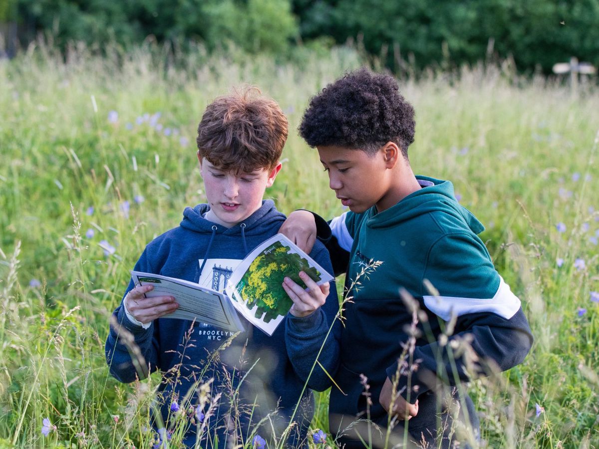 Two teenagers looking at booklet whilst stood in long grass