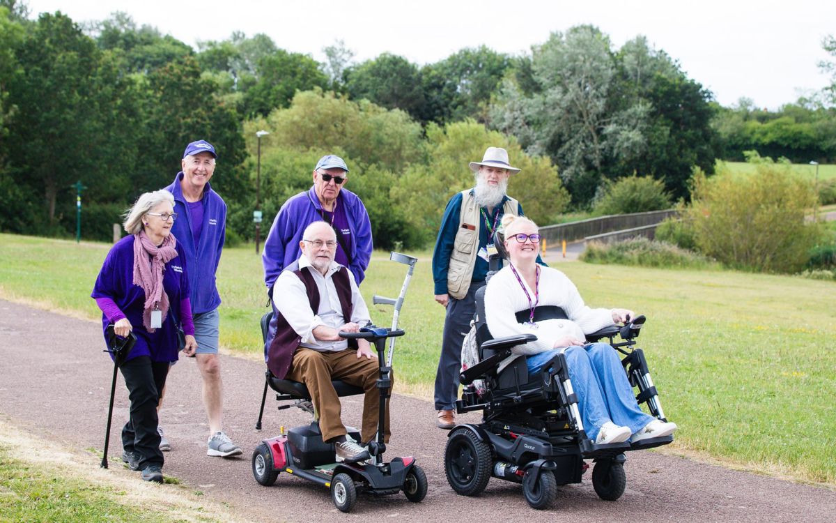 Group of travelling along on path in purple uniform and two in wheelchairs