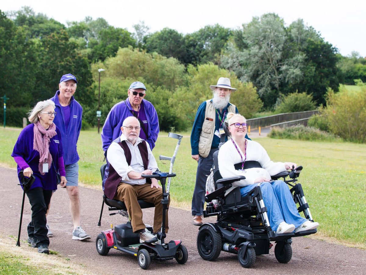 Group of travelling along on path in purple uniform and two in wheelchairs