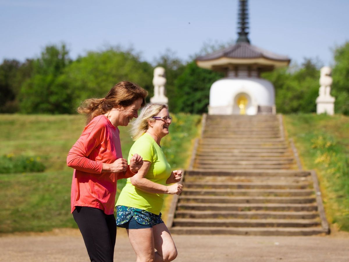 Two people running together at Willen Lake North with Peace Pagoda in the background