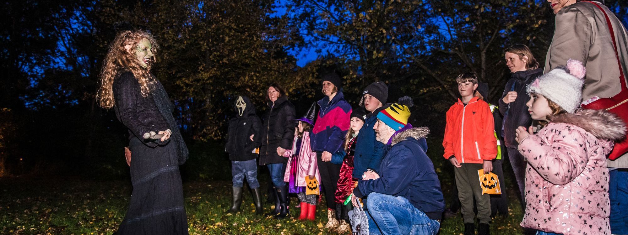 Storyteller with face painted in green, telling a story to the crown in a cold evening 