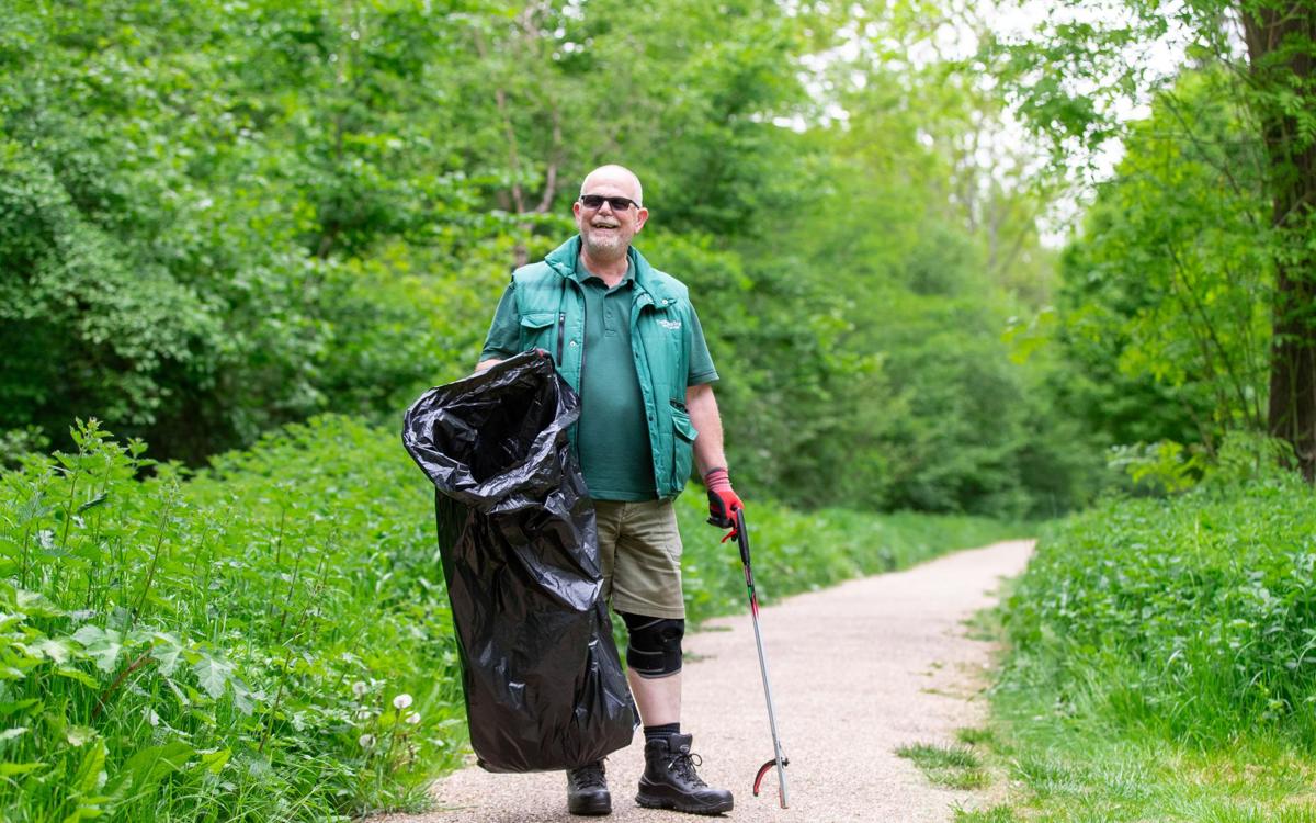Parks Trust staff member in green uniform holding bin bag and litter picker