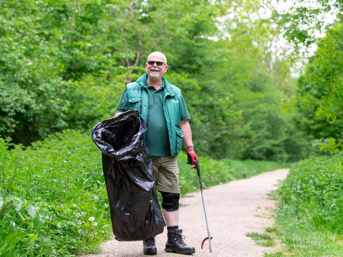 Parks Trust staff member in green uniform holding bin bag and litter picker