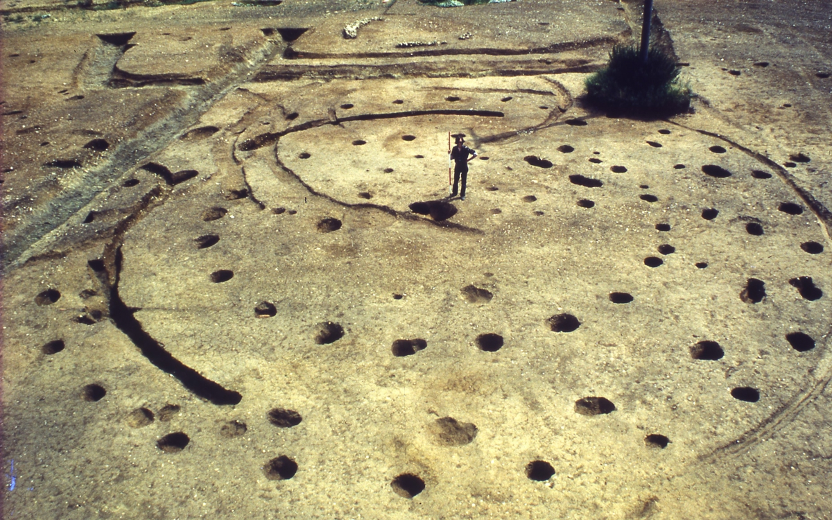 Photo of post holes of the round house with archaeologist shown for size