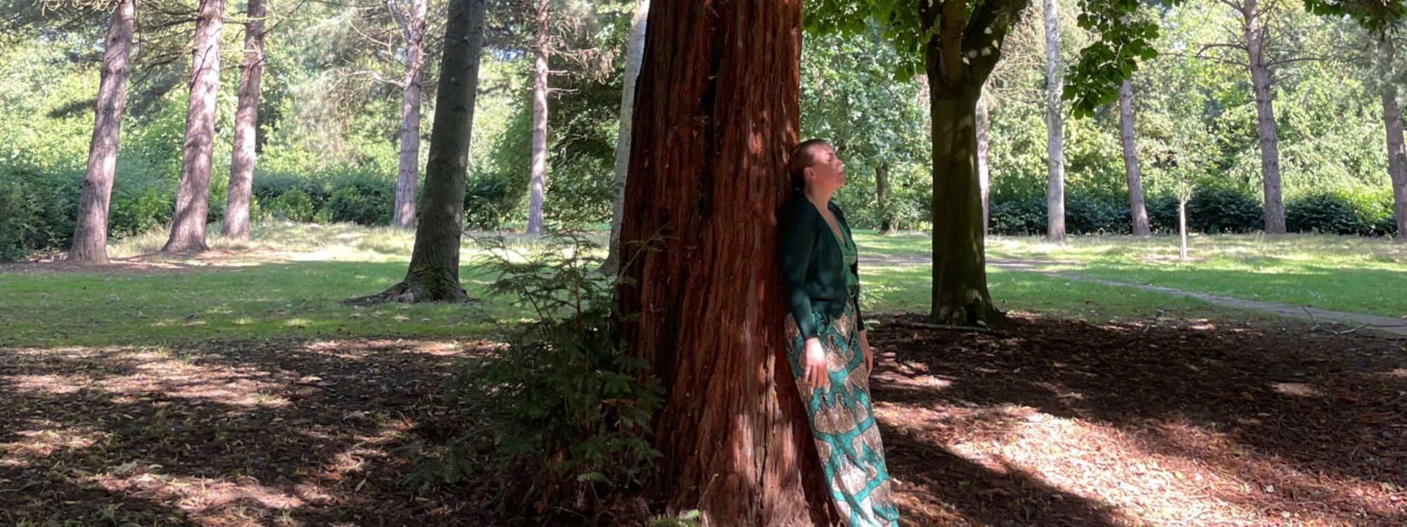 Person stood barefoot leaning on tree in the park