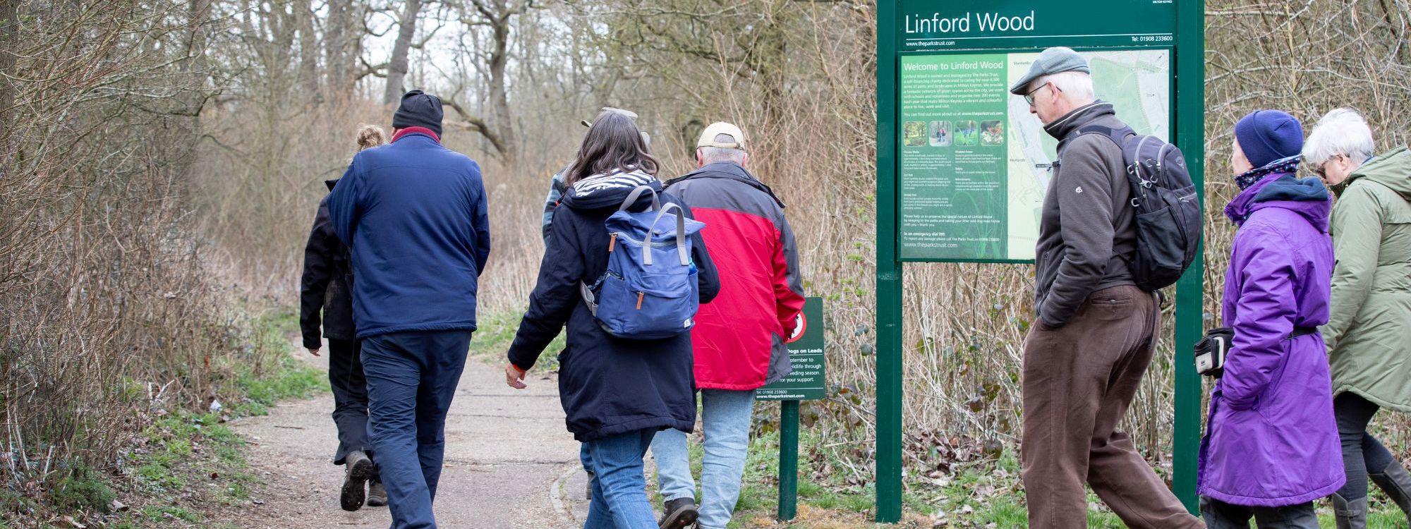 Group of people walking past Linford Wood welcome sign