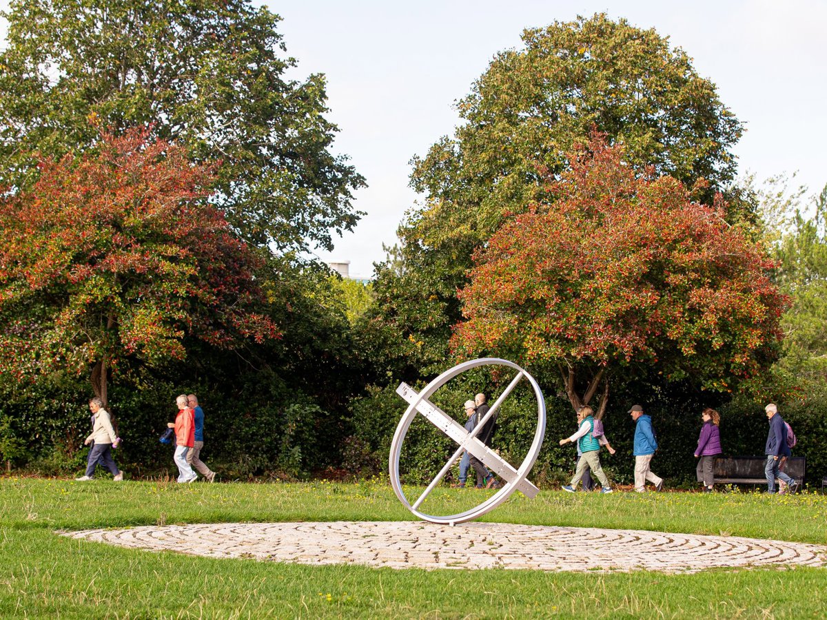 Group of people walking behind silver circular public art piece