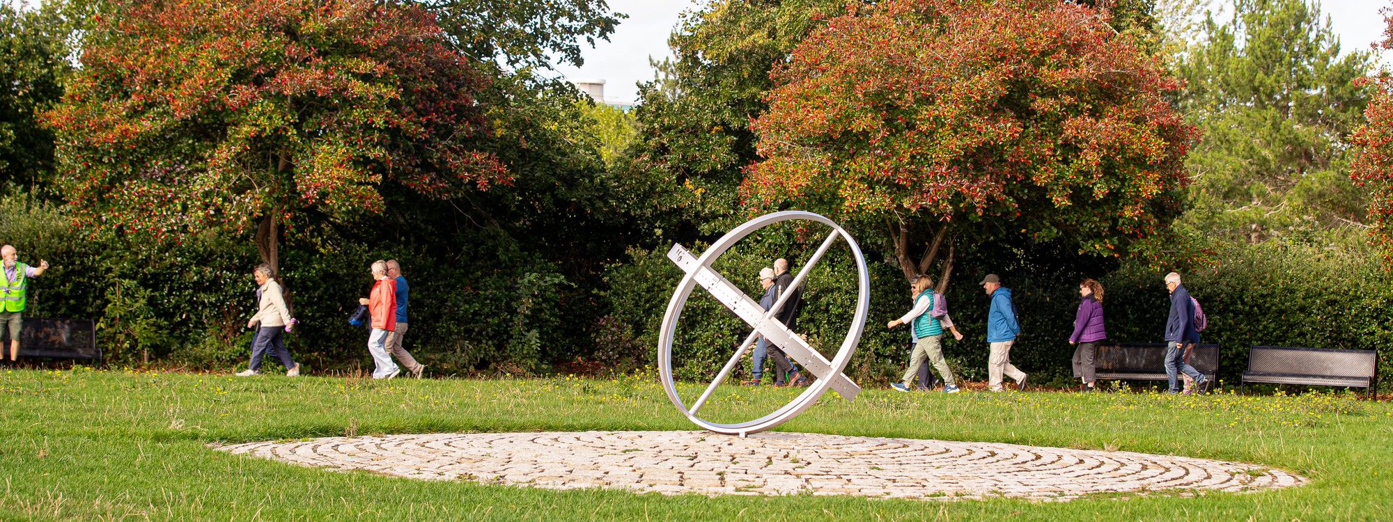 Group of people walking behind silver circular public art piece