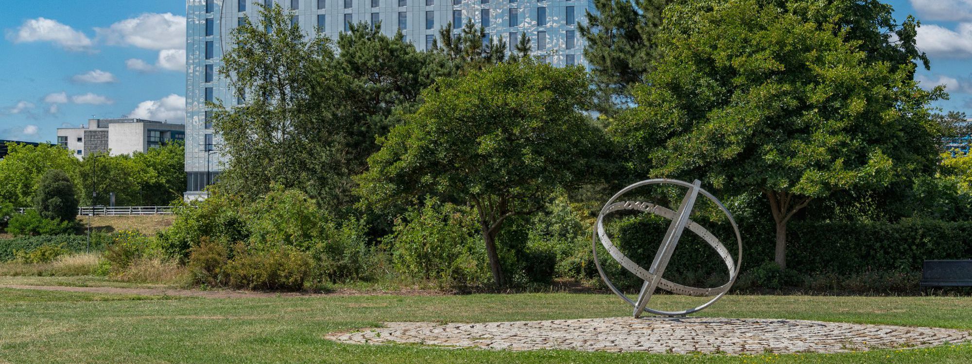 Armillary sphere public art made from metal with trees and mirrored hotel building in background
