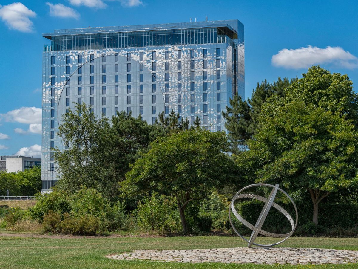 Armillary sphere public art made from metal with trees and mirrored hotel building in background