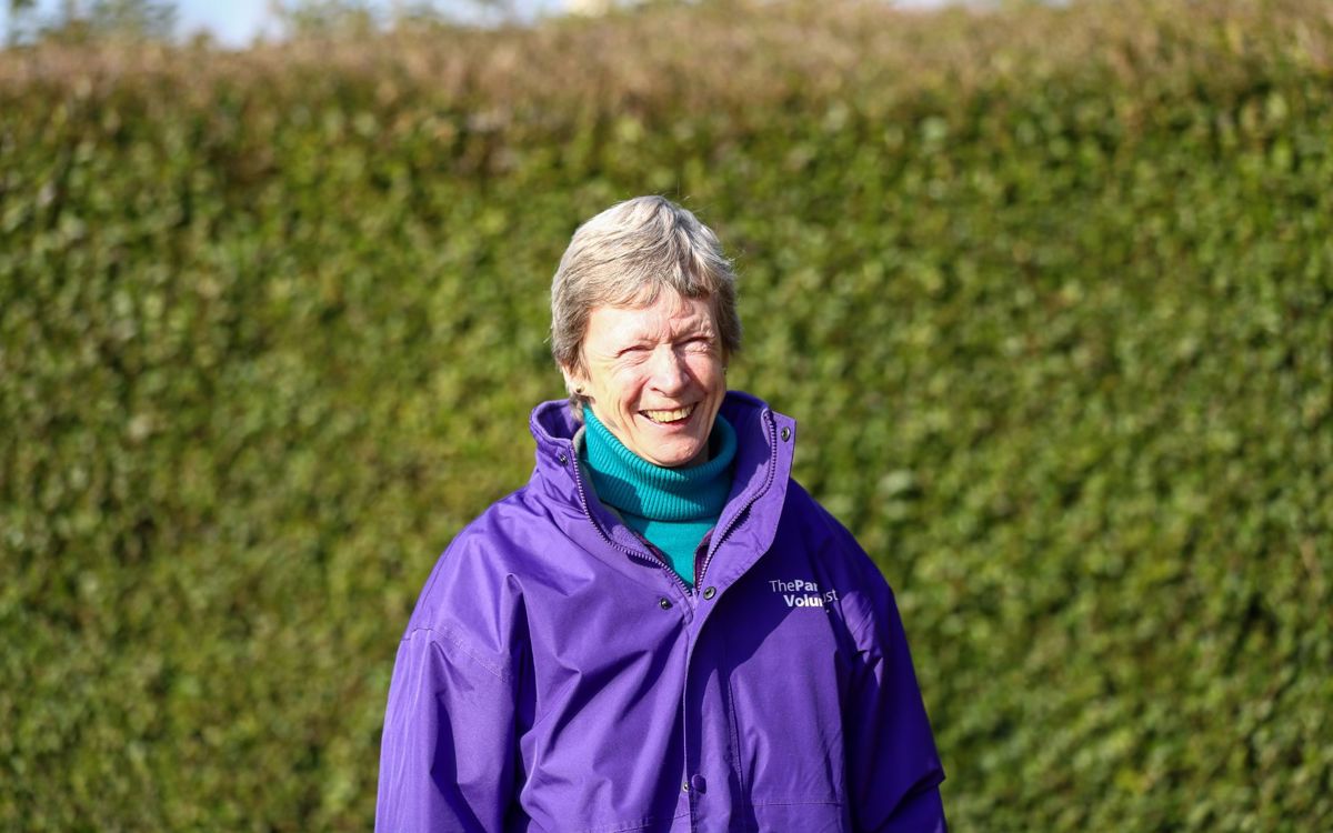 Person in purple Parks Trust uniform outdoors with greenery in background