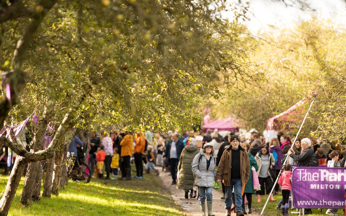 Couple walking in the mist of the crowd at the Apple Day event. The weather is sunny and there is a person with an apple picker.
