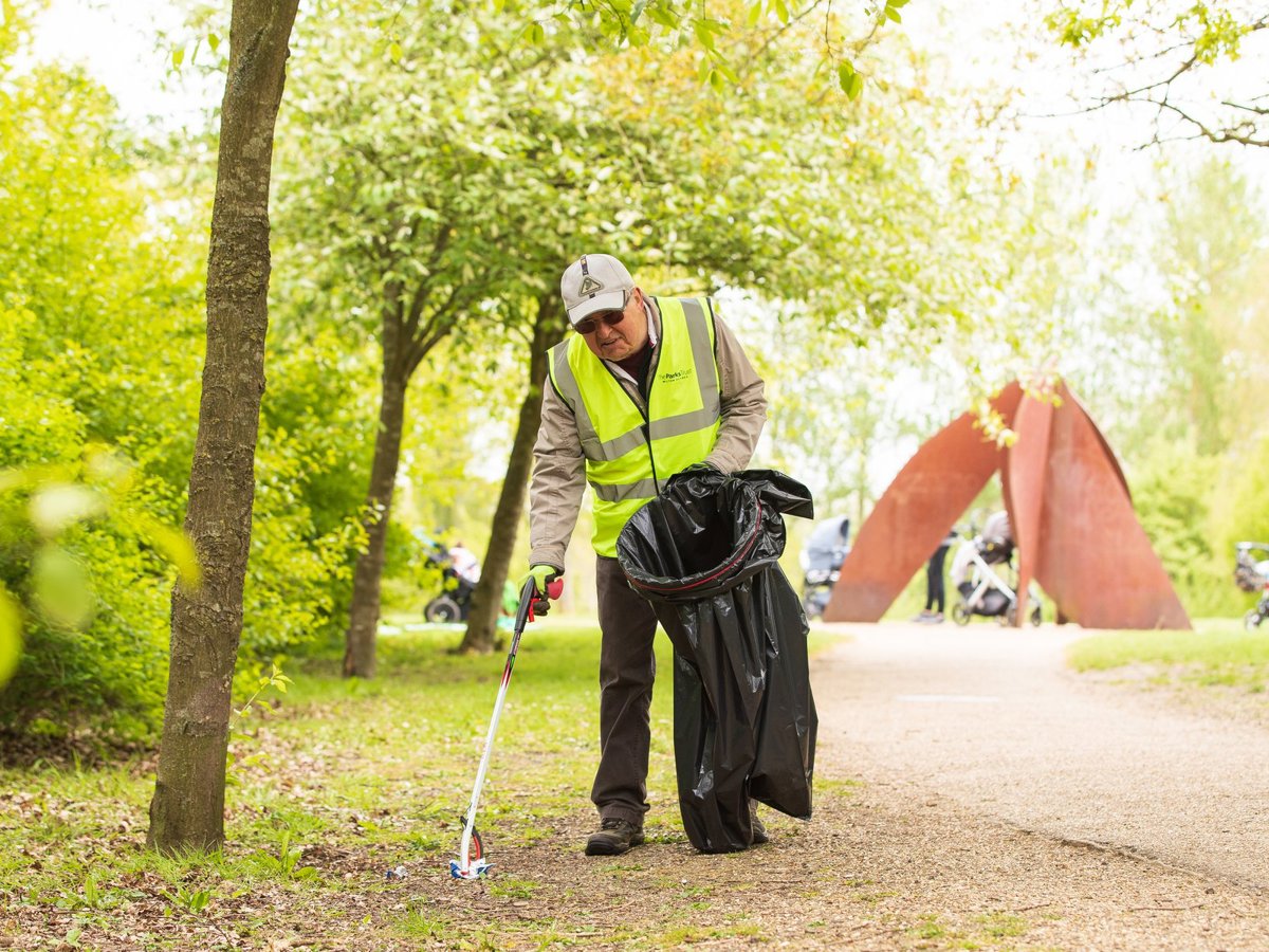 A volunteer in hivis litter picking in a parkland scene with a large public artwork in the background