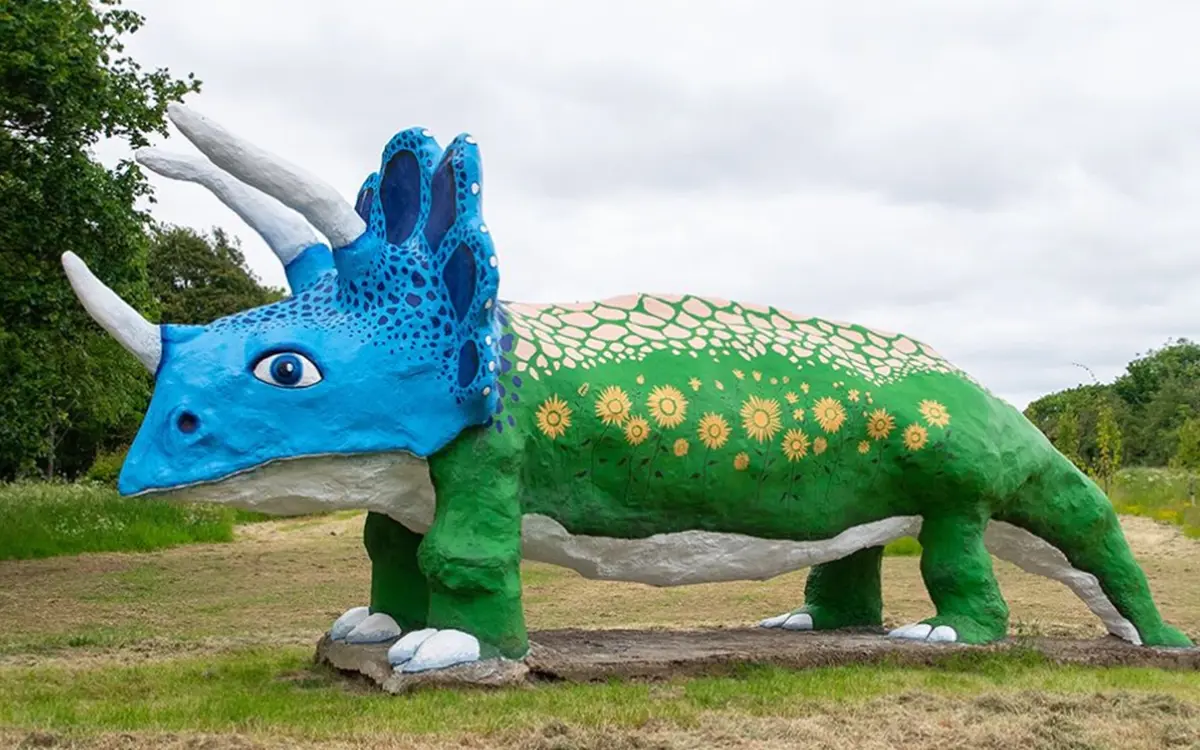 large triceratops the body is painted green with sunflowers dotted round which are yellow and the dinosaur has a blue head