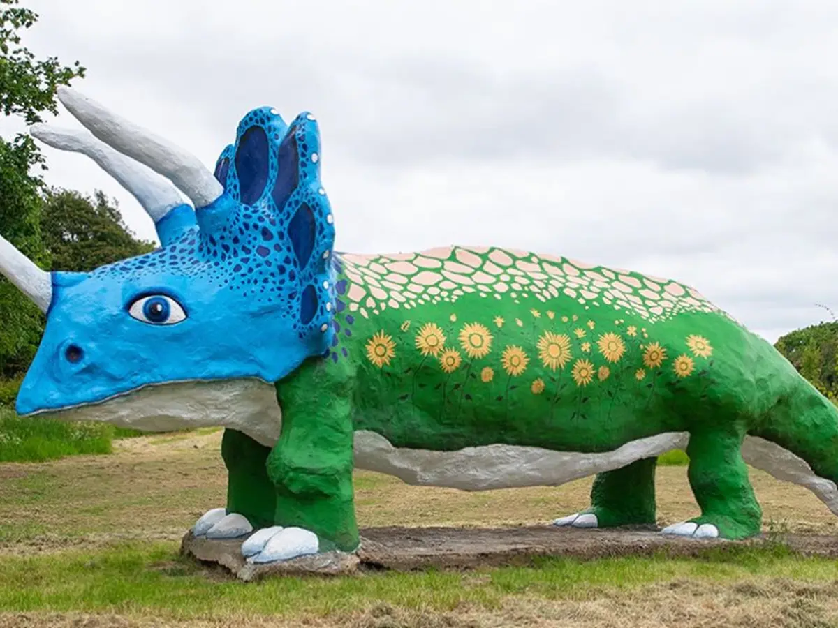 large triceratops the body is painted green with sunflowers dotted round which are yellow and the dinosaur has a blue head