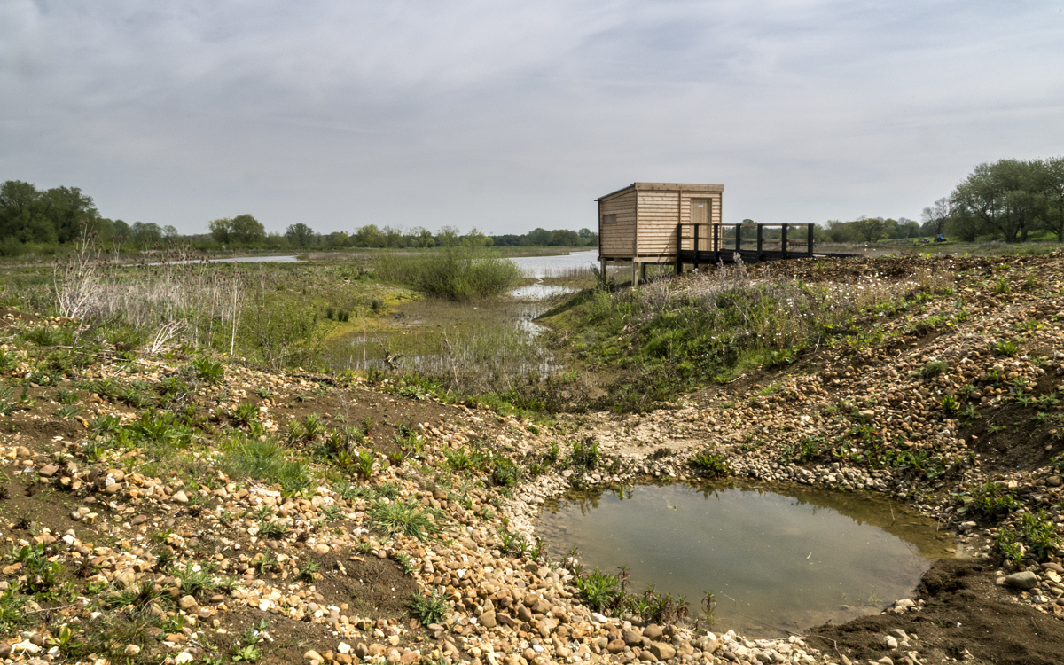 A bird hide surrounded by gravel and ponds