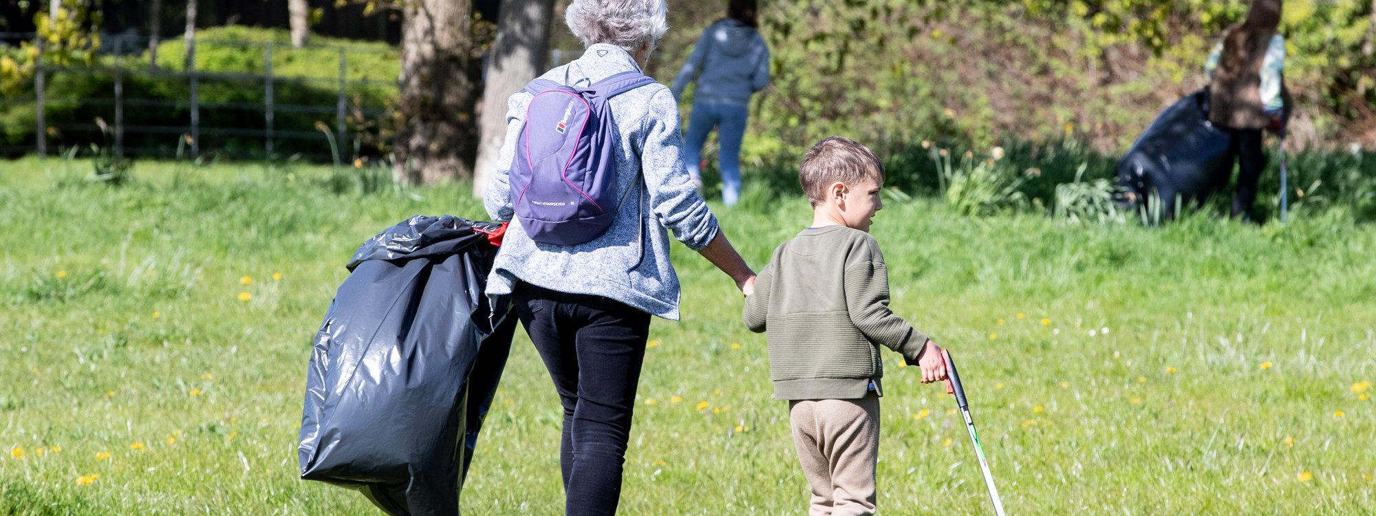 An older person and a younger person litter picking in a parkland scene