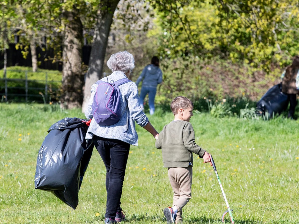 An older person and a younger person litter picking in a parkland scene