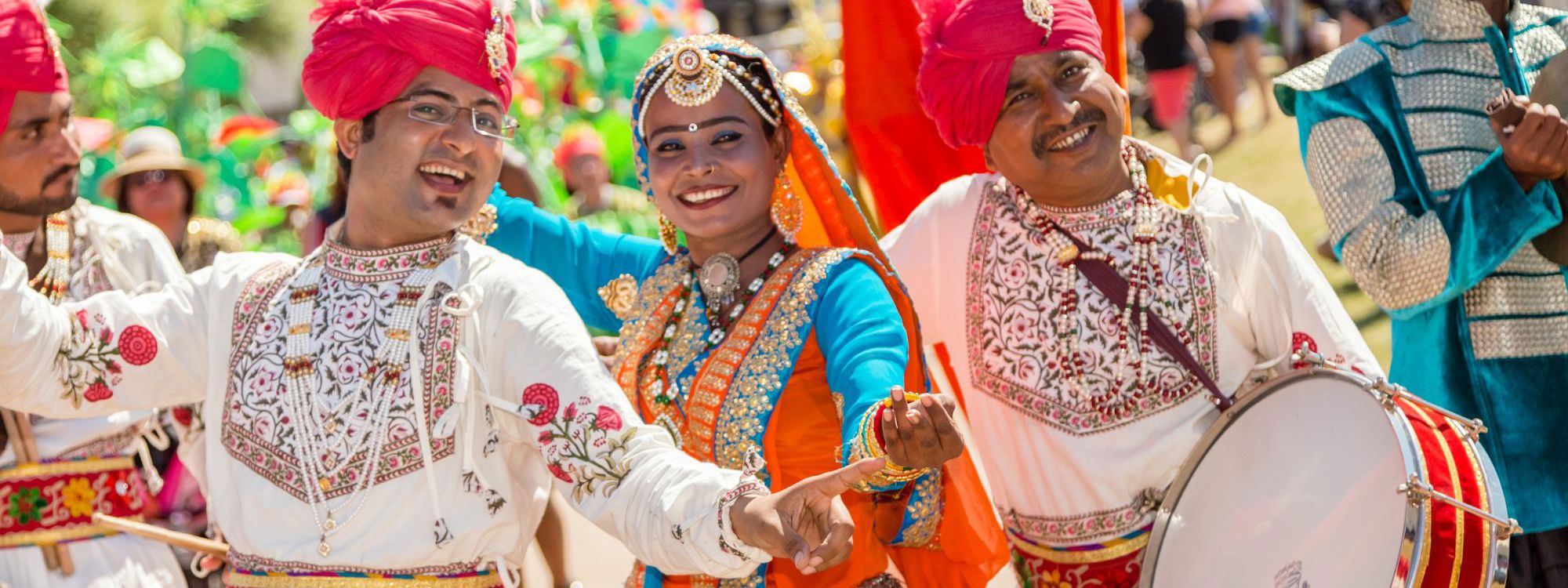 Three performers in colourful outfits smiling at the camera