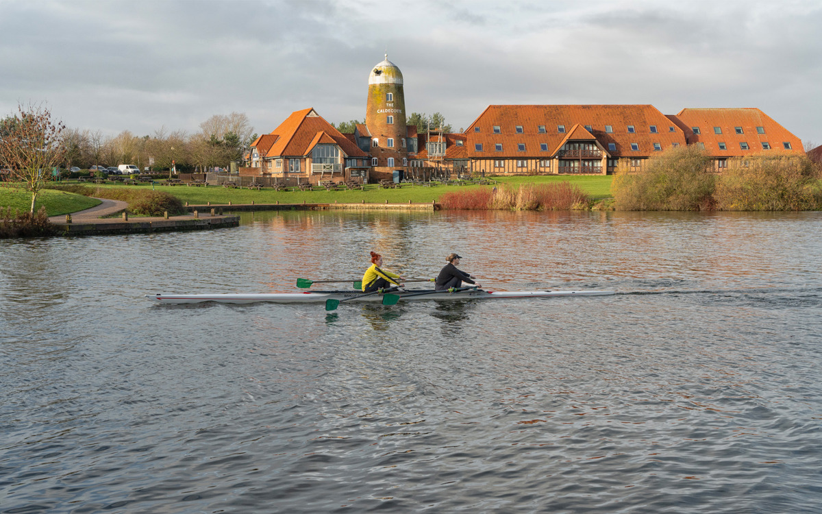 Pair of rowers on the water at Caldecotte Lake. Group of buildings in the background.