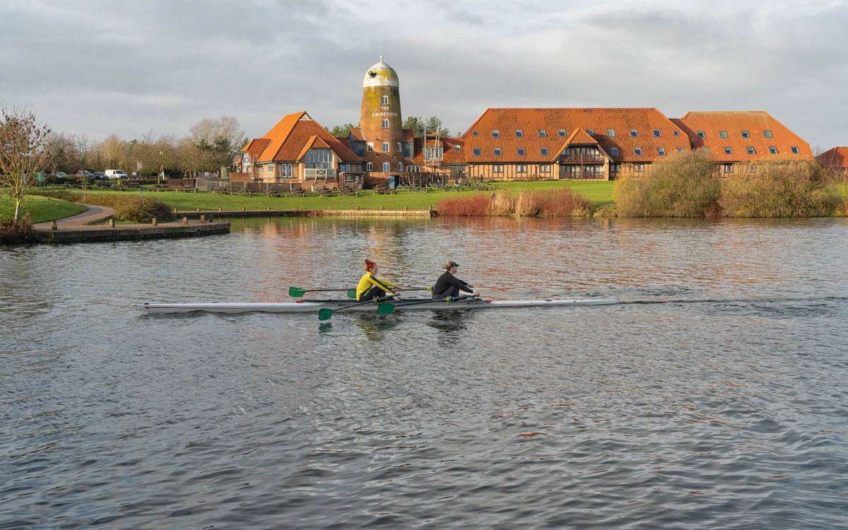 Pair of rowers on the water at Caldecotte Lake. Group of buildings in the background.