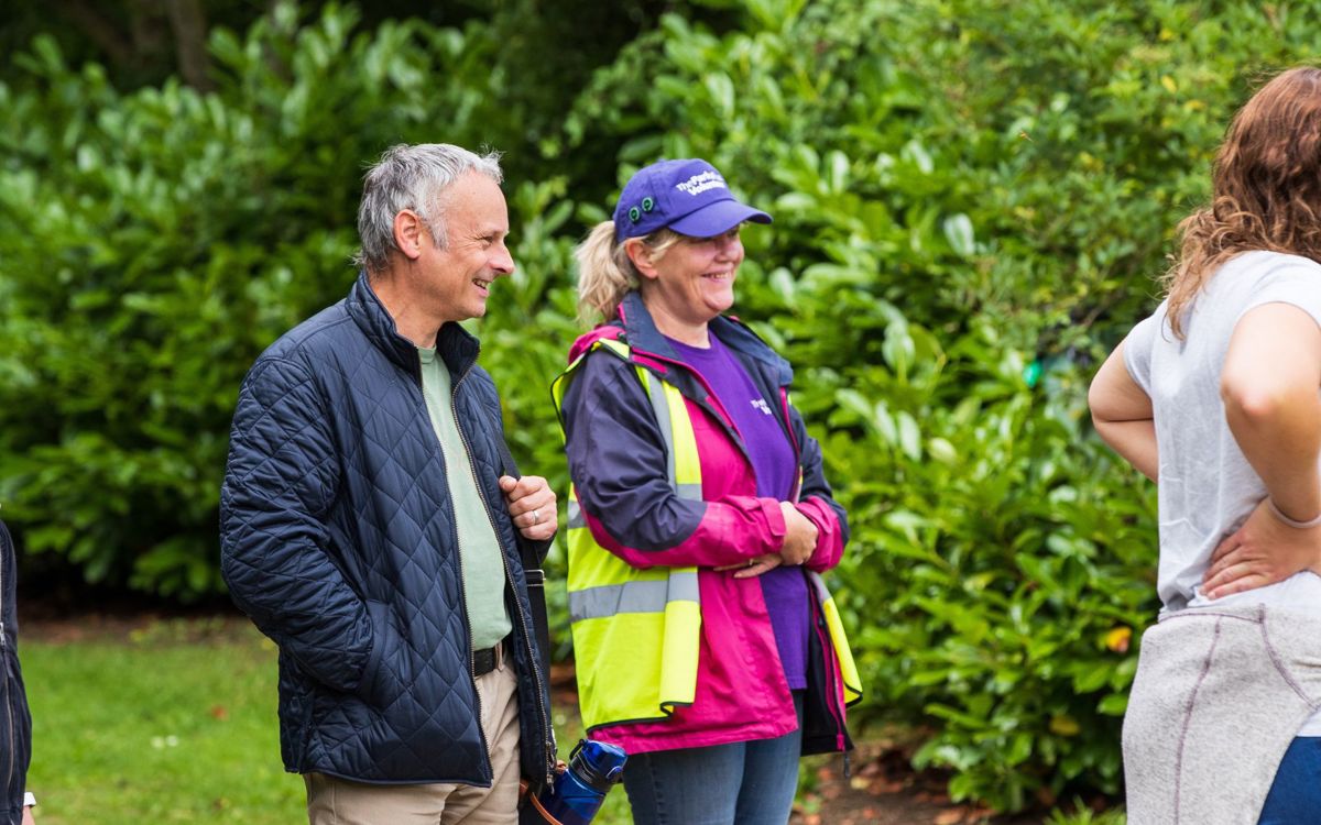 Julie Brady in purple cap and high vis with member of the public in the park