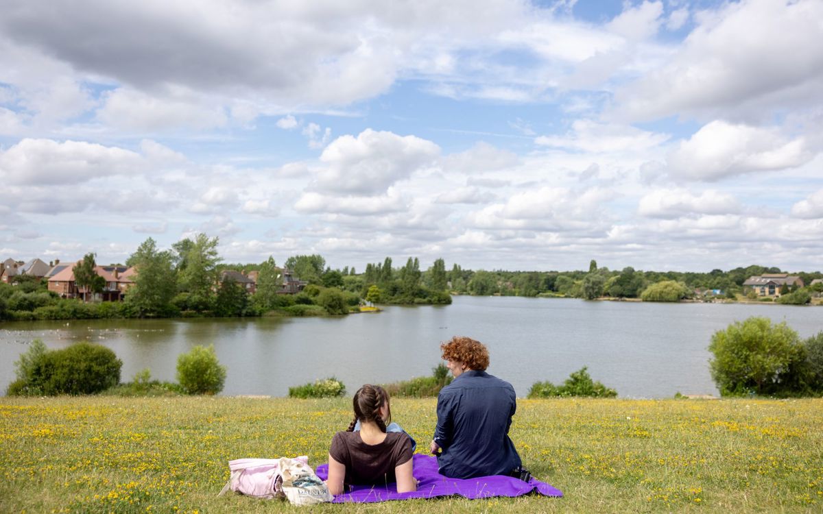Two teenagers sat on a blanket with lake infront