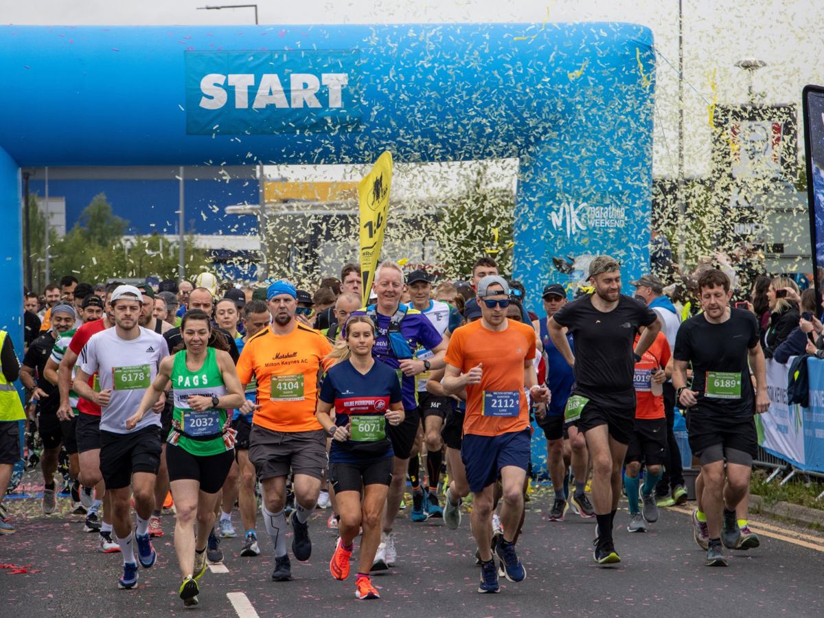 Marathon runners starting the run by passing through the blue inflatable start sign and a cloud of confetti.